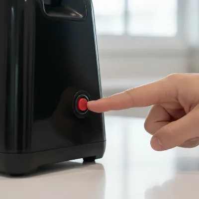 A close-up of a hand pressing a red reset button on the underside of a black electric meat grinder, illustrating the overload protector reset process.