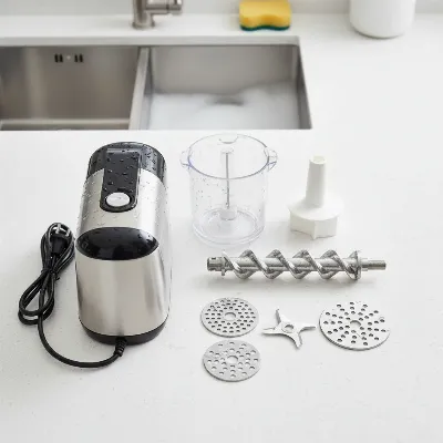 An electric meat grinder disassembled for cleaning, with various parts on a counter.